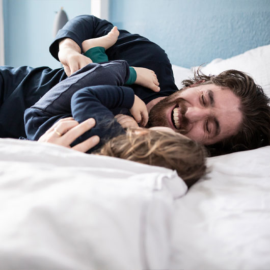 Vater und Kind toben im Schlafanzug im Bett