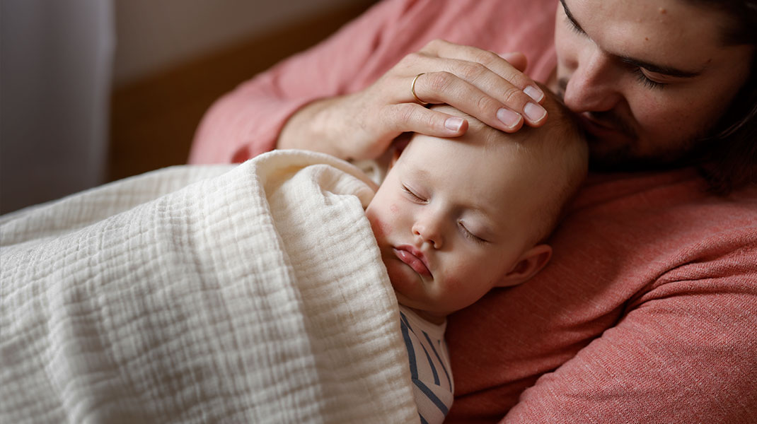 Baby schläft unter Bio-Musselintuch auf dem Bauch seines Vaters