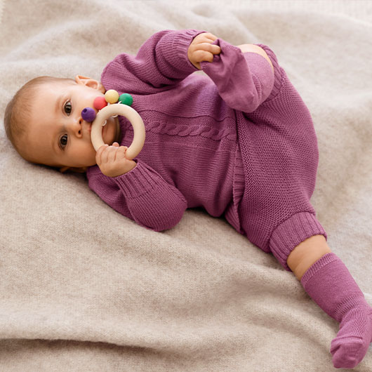 Baby in rosenholz-farbenem Schurwoll-Set von Waschbär spielt mit Holz-Beißring