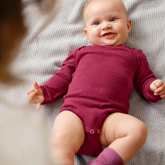 Baby in rotem Bio-Babybody aus Bourette-Seide