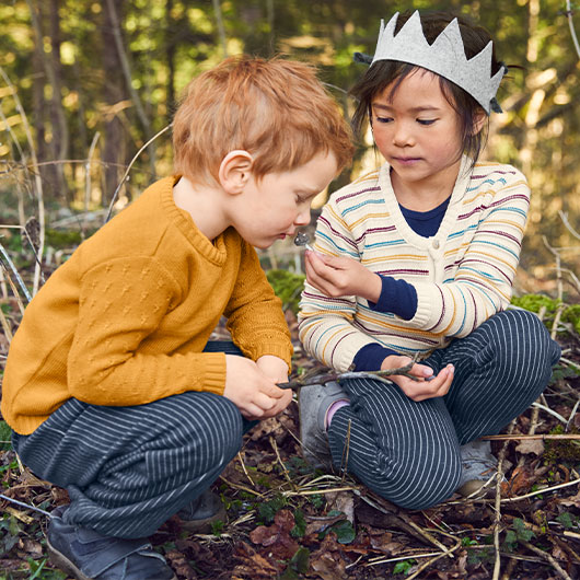 Junge und Mädchen in farbenfrohem und gemütlichem Pullover und Cardigan spielen im Wald