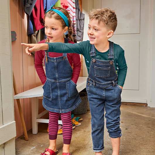 Junge und Mädchen in Jeans-Latzhose und Latzkleid im Flur