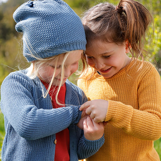 Junge und Mädchen in Cardigan und Pullover aus Bio-Baumwolle beobachten ein Insekt
