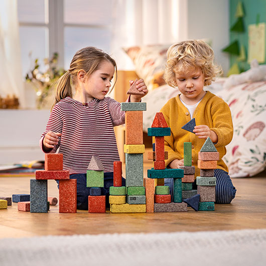 Mädchen und Junge spielen mit bunten Bausteinen und Bauklötzen aus Kork