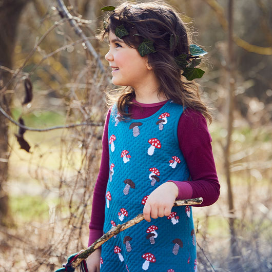 Mädchen in Wendekleid mit Pilzmotiv im Wald