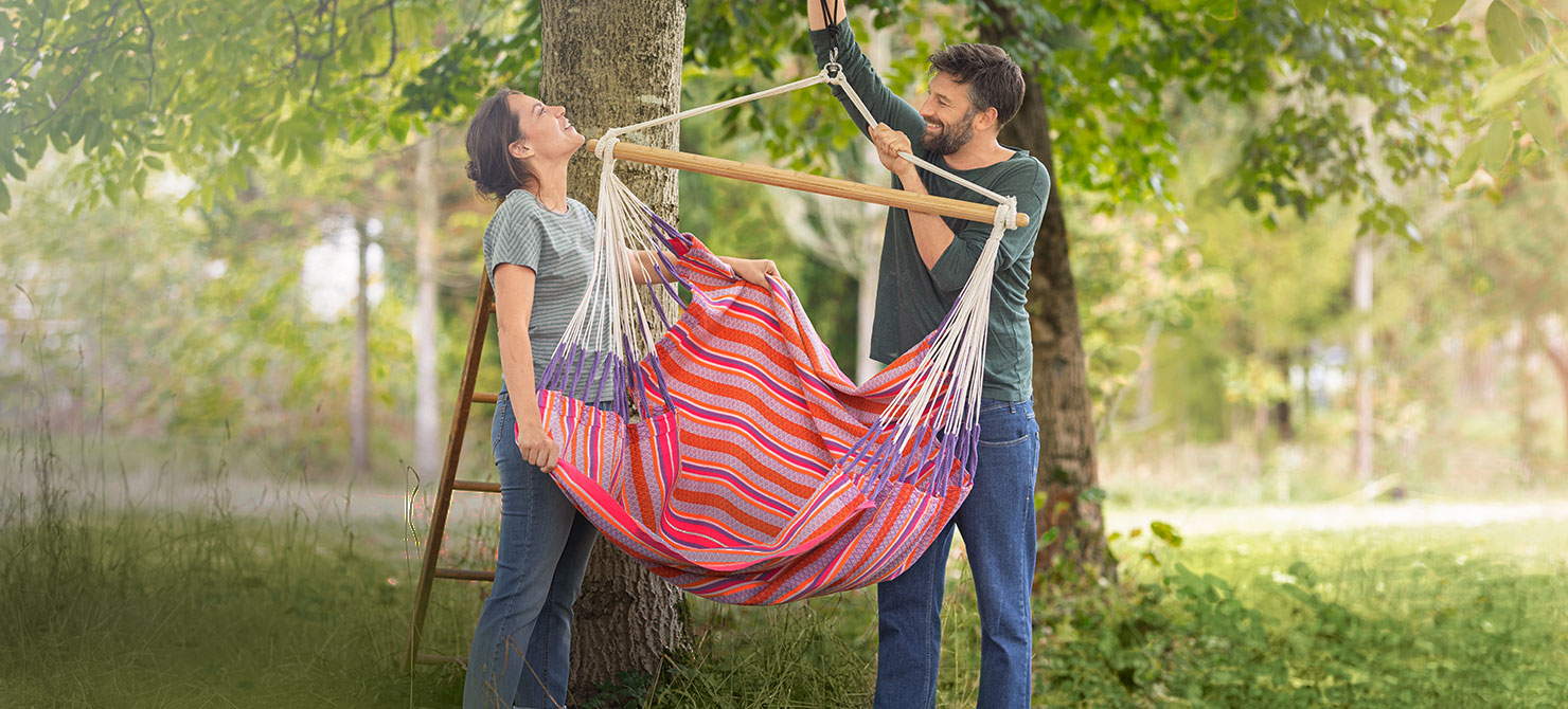 Frau und Mann befestigen Hängesessel in einem Baum im Naturgarten